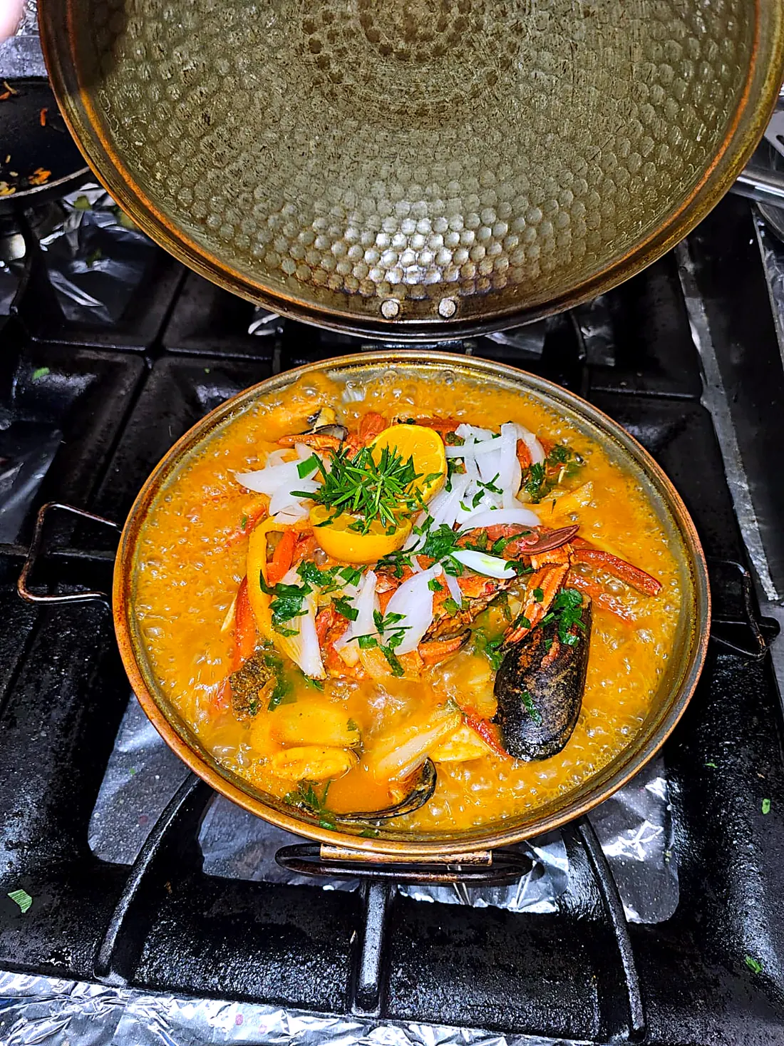 Geöffnete Kupfer-Cataplana auf dem Herd, mit Meeresfrüchten